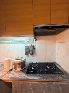 A kitchen with a Tixx gas stove, a kettle, and a rice cooker.
