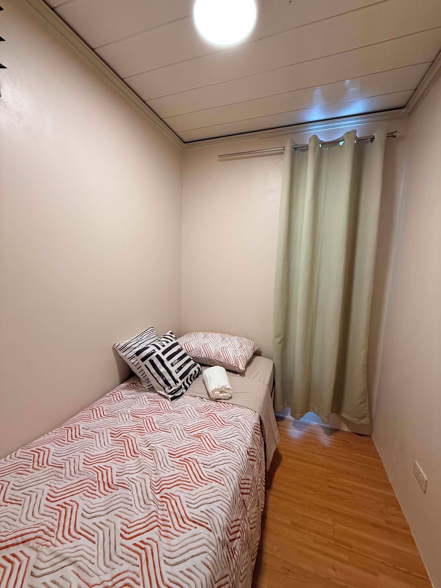 A small, single-bed room with a patterned bedspread, a pillow, and a bedside table.