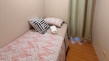 A small, single-bed room with a patterned bedspread, a pillow, and a bedside table.