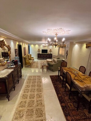 A spacious living room with a chandelier, a sofa, a coffee table, and a dining area with chairs and a table. - Vintage 2-Bedroom Apartment with AC & Large Balcony in Giza (Giza Governorate)