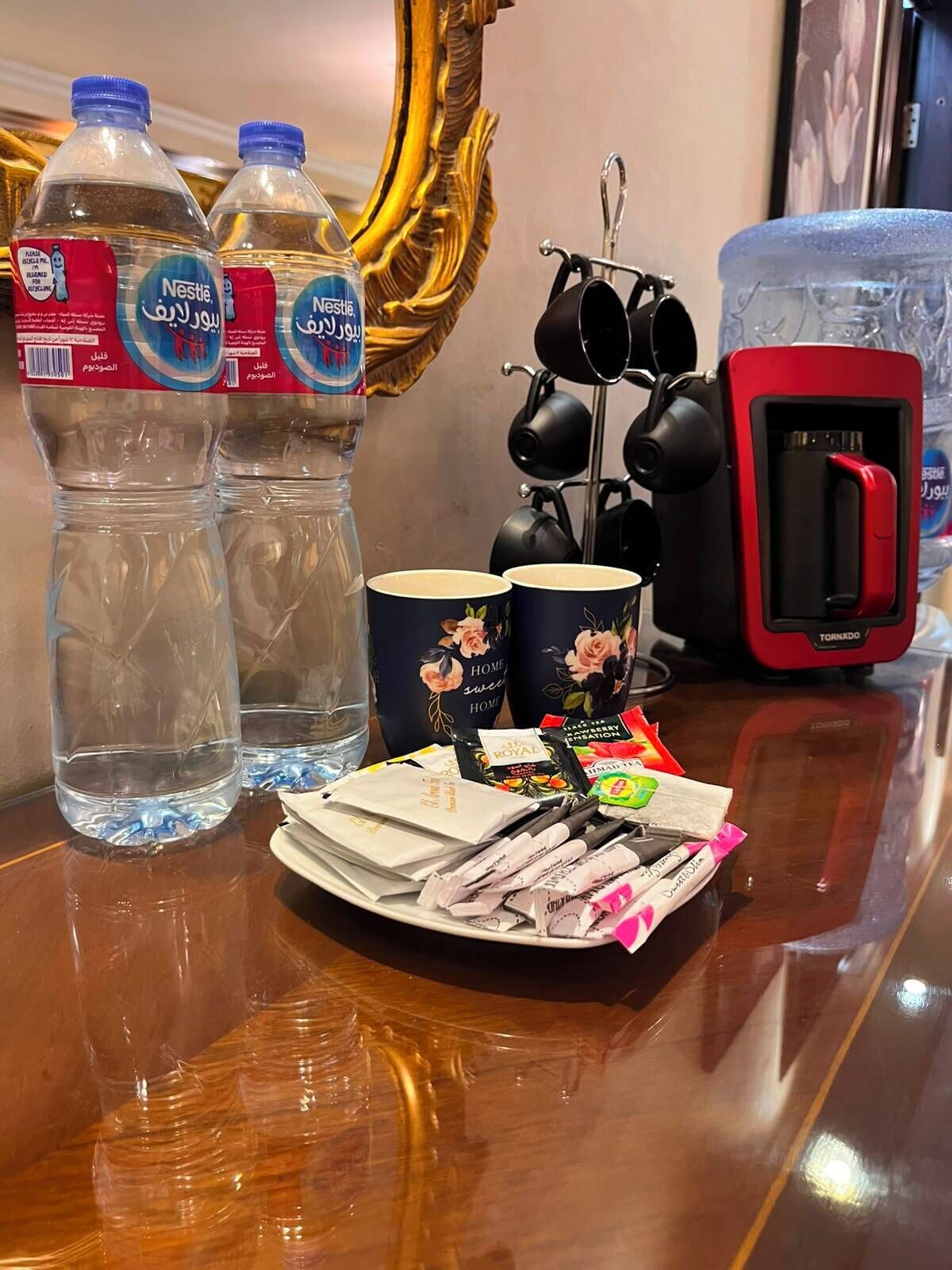 A table with two Nestlé water bottles, a red portable charger, a tea kettle, a plate of snacks, and a decorative item.