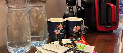 A table with two Nestlé water bottles, a red portable charger, a tea kettle, a plate of snacks, and a decorative item.