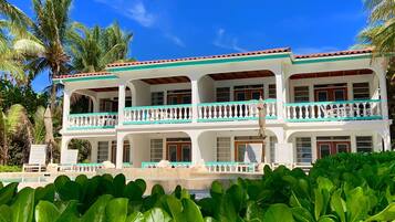 A two-story building with a balcony, surrounded by lush greenery and palm trees.