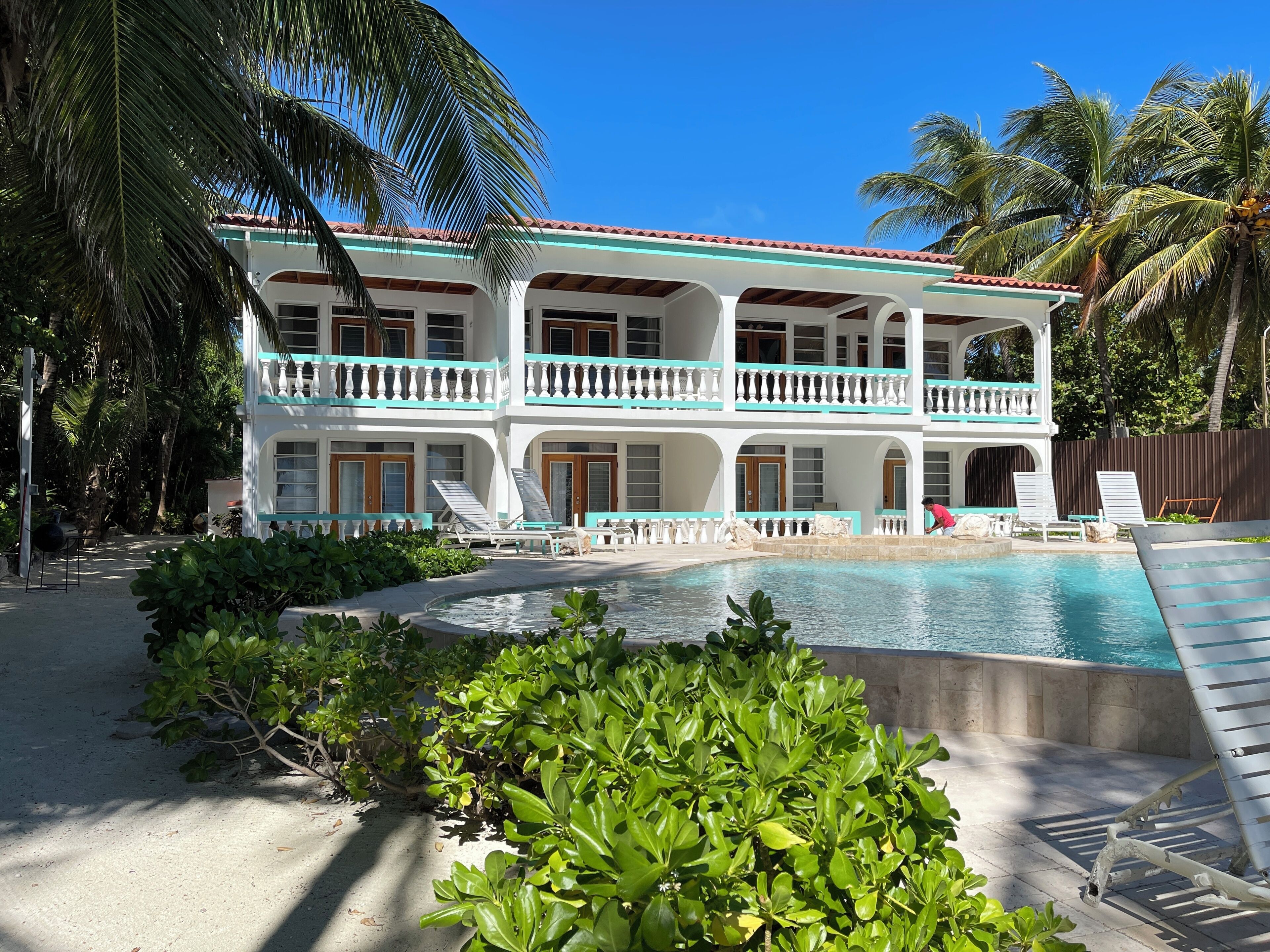A two-story building with a pool, surrounded by palm trees and greenery.