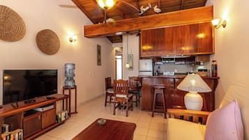 A living room with a TV, wooden furniture, a water dispenser, and a kitchen area with wooden cabinets and a bar.