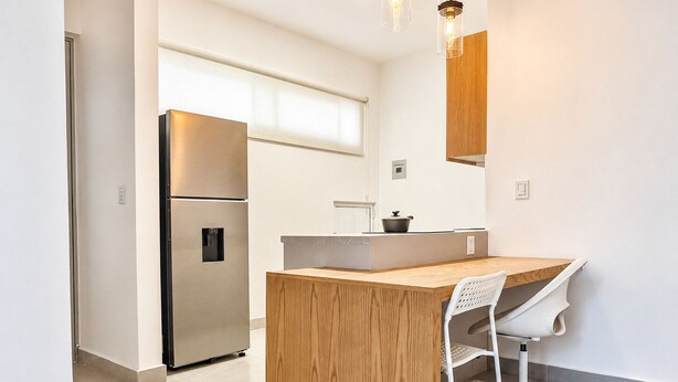A modern kitchen with a built-in island, stainless steel refrigerator, and white cabinetry.