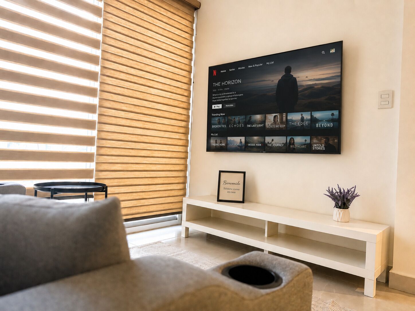 Een moderne woonkamer met een grote flatscreen televisie aan de muur, een witte console tafel en een grijze bank.