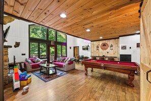 Een kamer met een pooltafel, banken en een groot raam.