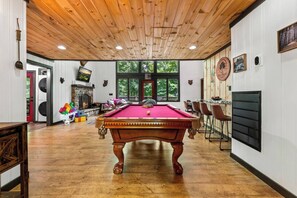 Een pooltafel in een ruimte met houten vloeren, een open haard en een groot raam.