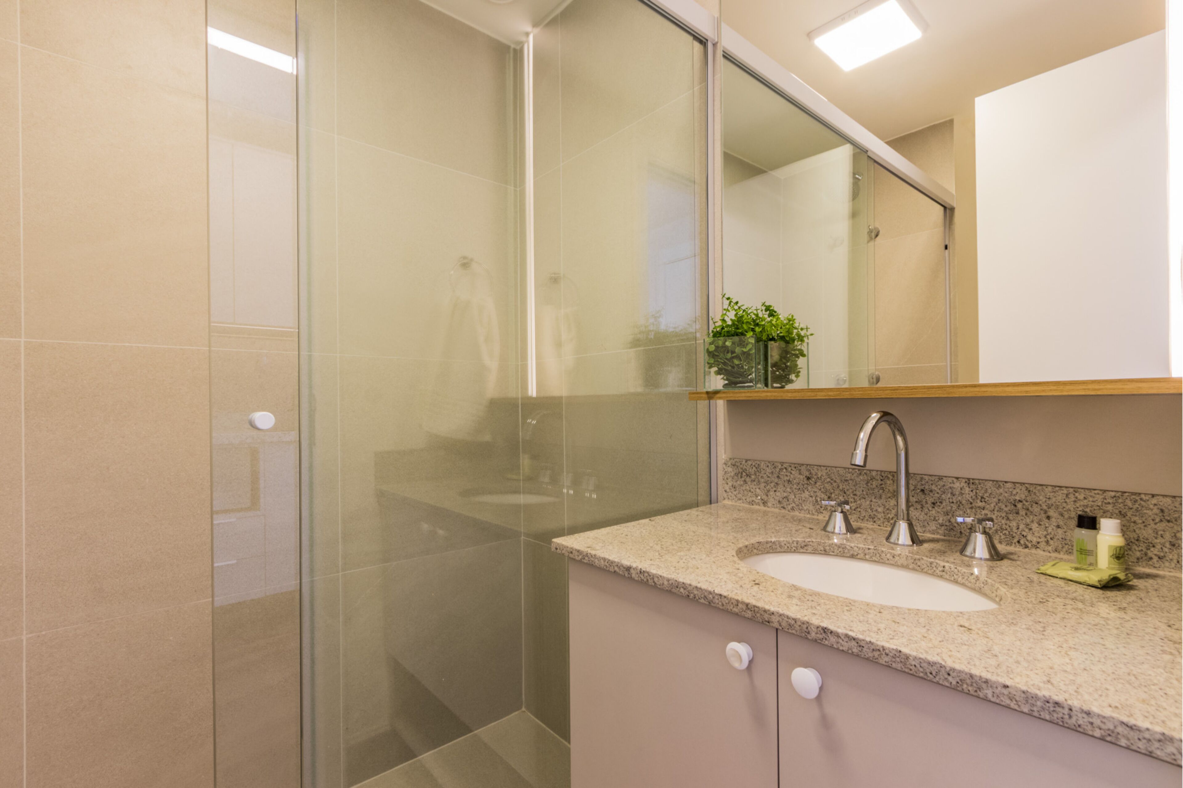 Un baño moderno con cabina de ducha de vidrio, encimera de granito y espejo sobre el lavabo.