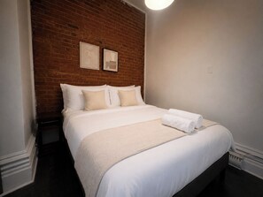 Habitació d'hotel amb paret de maó, llit amb roba de llit blanca i dos quadres a la paret.
