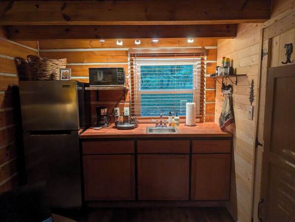 A compact kitchen with a refrigerator, microwave, coffee maker, and a window with blinds.