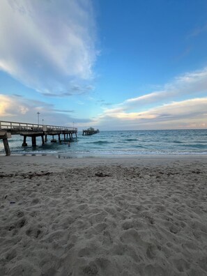 Ein Strand mit einer Mole, die sich ins Wasser erstreckt, einem klaren Himmel und ruhiger See.