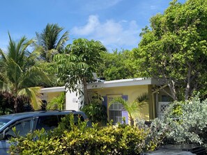 A two-story building with a yellow facade, a car parked in the driveway, and lush greenery surrounding the property. - Charming BEACH apartment in Fabulous Lauderdale-by-the-Sea (Lauderdale-by-the-Sea)