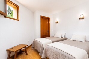 Ein Zimmer mit zwei Betten, einer Holztür, einem kleinen Tisch und einem Fenster.