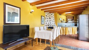 A living room with a television, a dining table with chairs, a kitchen in the background, and a ceiling with wooden beams. - Home2Book Icod Terrace, BBQ & Nature (Icod de los Vinos)