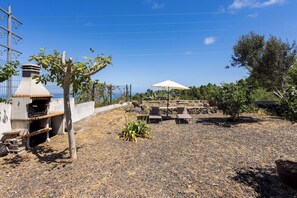 Een terras buiten met een barbecue, zithoek en uitzicht op zee.