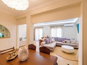 A modern living room with a sofa, coffee table, and dining area with chairs and a table. - Ivelia Athens - Boutique Residence with Private Spa (Athina)
