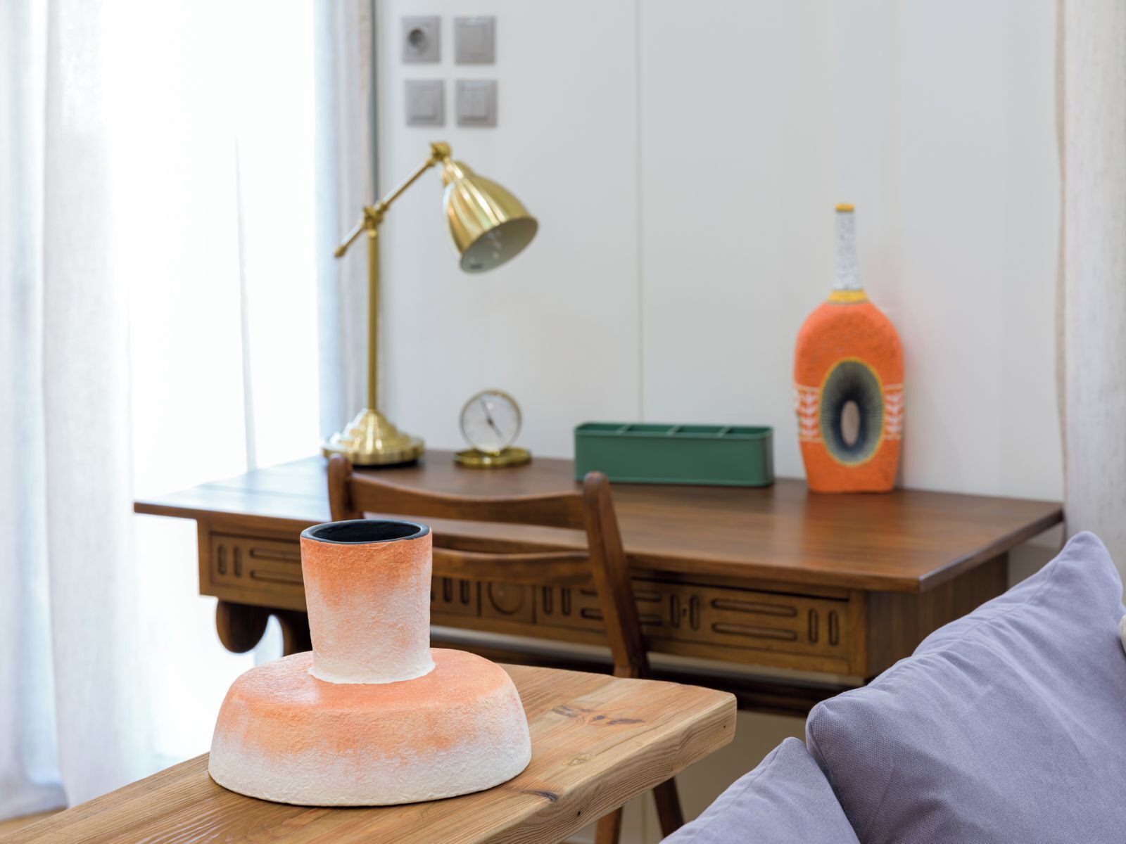 Een houten tafel met een vaas, een lamp, een klok en een fles op een houten stoel.