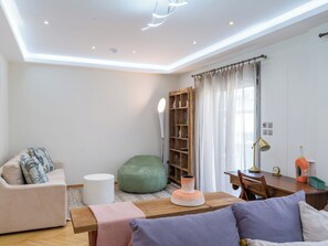 Ein modernes Wohnzimmer mit einer Couch, einem grünen Sitzsack, einem Couchtisch aus Holz und einem Essbereich mit Tisch und Stühlen.