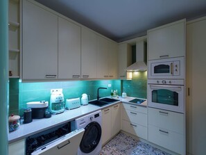 Une cuisine compacte avec des meubles blancs, un lave-vaisselle, un lave-linge, un évier et un four double.