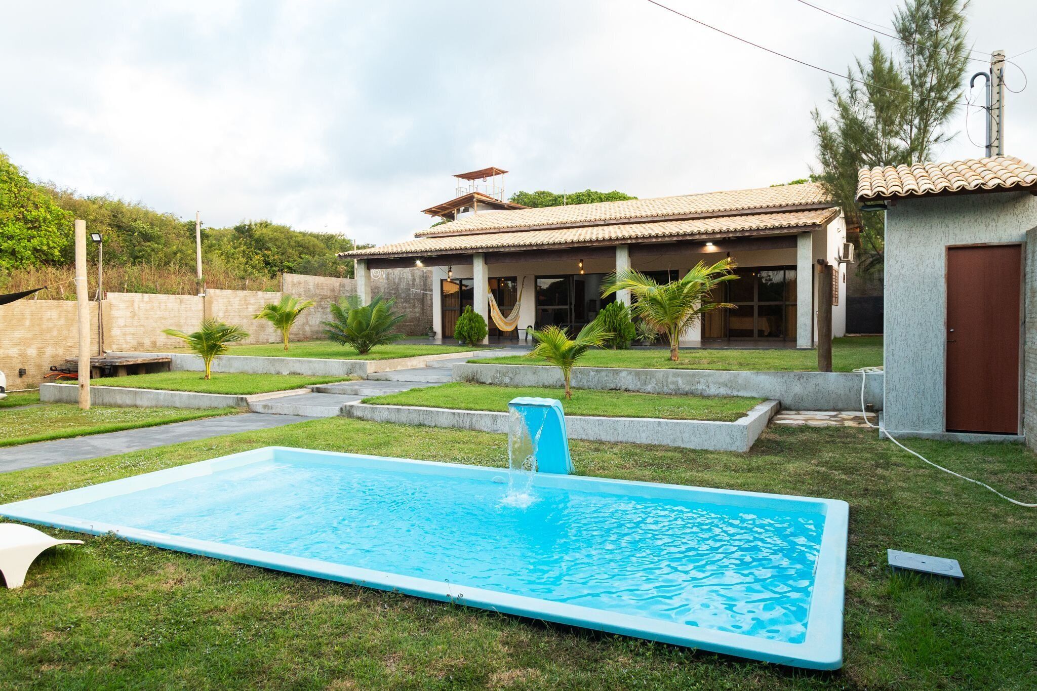 Una propiedad residencial con piscina, patio cubierto y un pequeño jardín de palmeras.