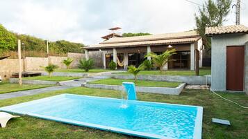 Una propiedad residencial con piscina, patio cubierto y un pequeño jardín de palmeras.