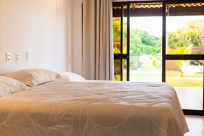 A bedroom with a large bed, a window with curtains, and a view of greenery outside. - Casa 2 suites-piscina priv-Picos161m (Icapuí)