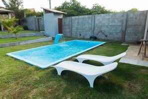 A rectangular swimming pool with a slide, two white lounge chairs, and a concrete wall in the background. - Casa 2 suites-piscina priv-Picos161m (Icapuí)