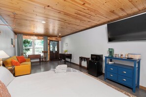 Una habitación de hotel con cama, sofá, televisión, escritorio y cómoda azul.