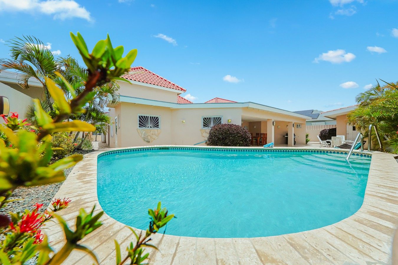 A swimming pool with a wooden deck, surrounded by buildings with red roofs and a clear blue sky.