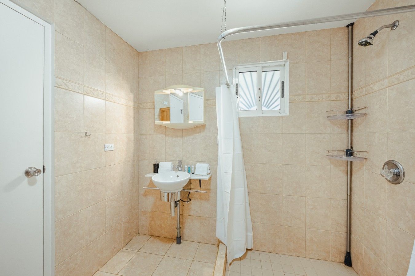 Un espacio de ducha pequeño y cerrado, con un lavamanos y un espejo blancos, un cabezal de ducha y una cortina.