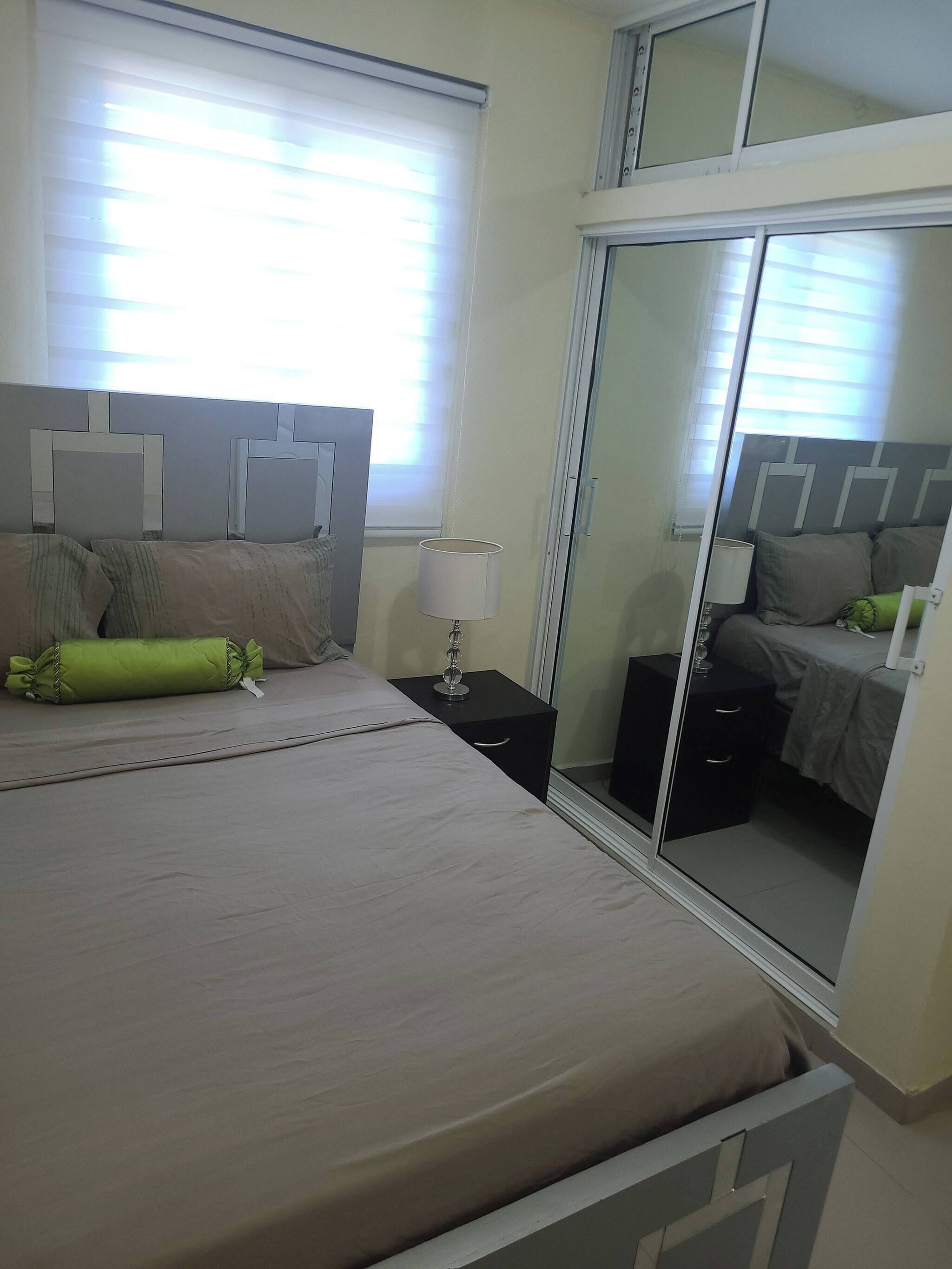 A hotel room with a bed, bedside tables, a lamp, and a mirror.