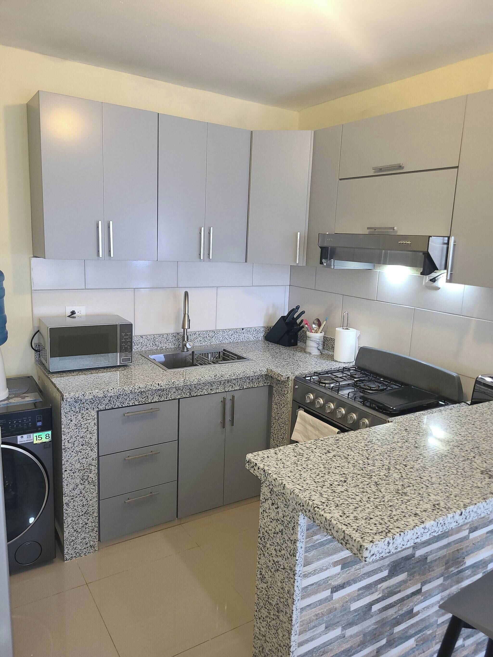 Cucina con mobili grigi, un piano di lavoro in granito, un fornello e un forno a microonde.