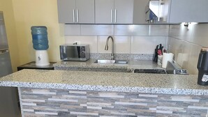 A kitchen with granite countertops, a microwave, a sink, and two bar stools. - Apartment for Rent ,3rd Floor (San Pedro de Macoris)