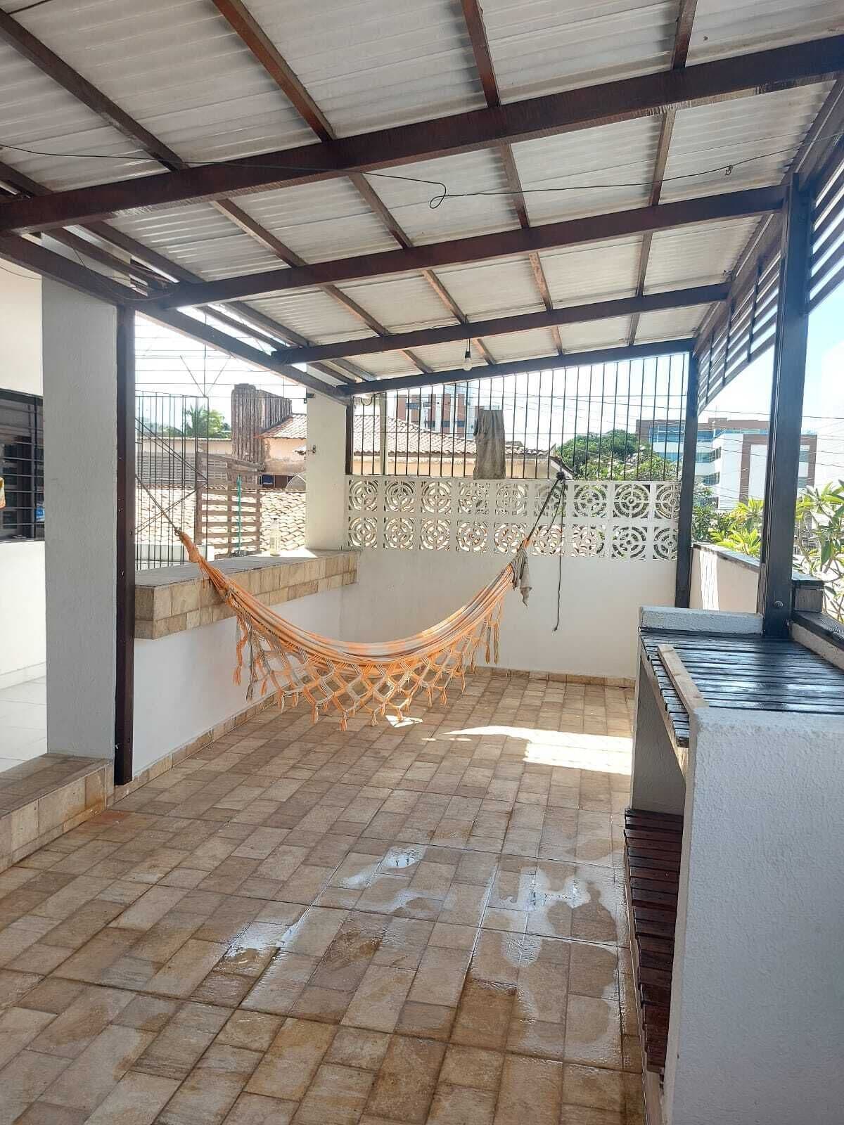 Uma área externa coberta com uma rede, piso de azulejos e vista para edifícios ao fundo.