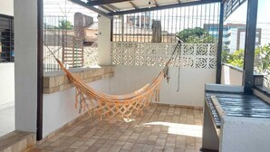 Un espacio al aire libre cubierto con una hamaca, piso de baldosas y vista de edificios al fondo.
