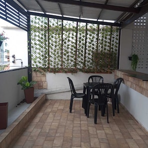 Un espace extérieur abrité, aménagé avec une table et des chaises, un pot de fleurs et un mur en treillis recouvert de plantes grimpantes.
