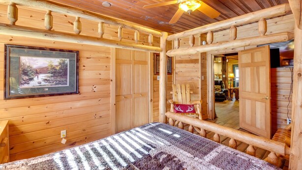 L’intérieur d’une cabane en rondins, avec un lit, un ventilateur de plafond, un tableau encadré et une porte donnant sur une autre pièce.