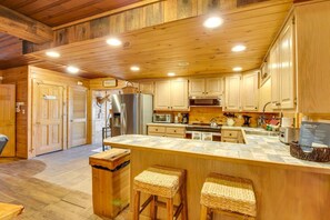 A wooden cabin interior with a kitchen featuring a refrigerator, stove, and wooden cabinets. - Riverfront Helen Cabin  Hot Tub + Fire Pit (Helen)