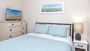 Quarto com cama, cômoda, mesa de cabeceira, abajur e um quadro na parede.