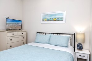 Ein Schlafzimmer mit Bett, Schminktisch, Nachttisch, Lampe und einem Bild an der Wand.