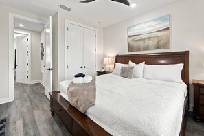 A bedroom with a large bed, a nightstand, a wall-mounted lamp, and a painting. - River District Residence | Walk to Armature Works | 3BR Townhome with Garage & Private Yard (Tampa)