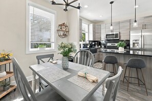 A modern kitchen with a central island, stainless steel appliances, and a dining area with a table set for four. - River District Residence | Walk to Armature Works | 3BR Townhome with Garage & Private Yard (Tampa)