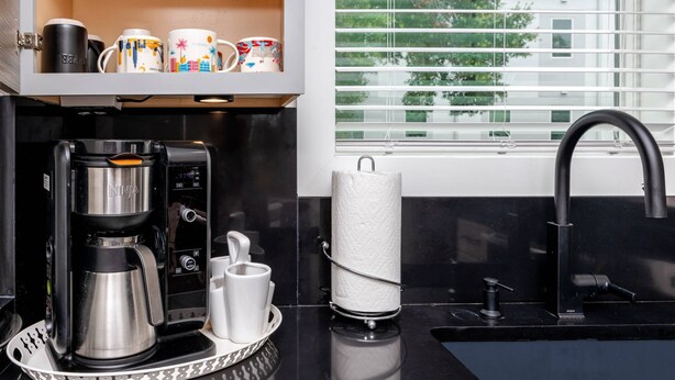 Cozinha com cafeteira, suporte para papel toalha e janela com persianas.