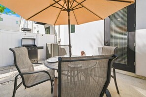 An outdoor patio with a round table, four chairs, a grill, and a large umbrella. - River District Residence | Walk to Armature Works | 3BR Townhome with Garage & Private Yard (Tampa)