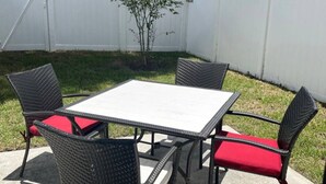 Pátio com mesa quadrada e quatro cadeiras com almofadas vermelhas.