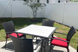 Eine Terrasse mit einem quadratischen Tisch und vier Stühlen mit roten Kissen.