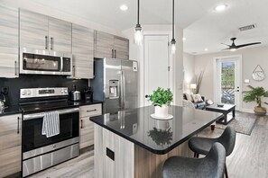 A modern kitchen with stainless steel appliances, a central island, and a dining area with a view. - River District Residence | Walk to Armature Works | 3BR Townhome with Garage & Private Yard (Tampa)
