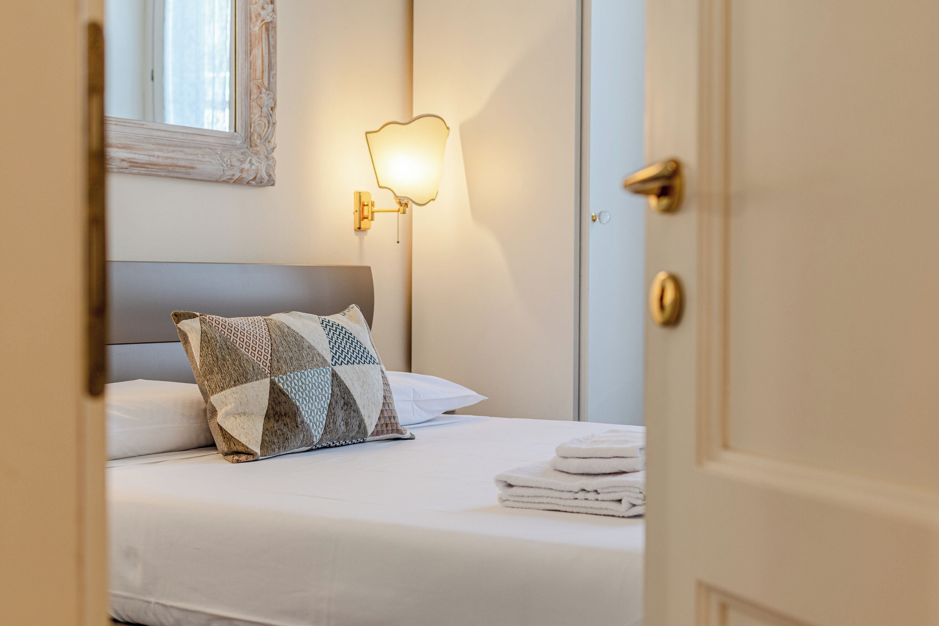 A hotel room with a neatly made bed, a wall-mounted light fixture, and a door.